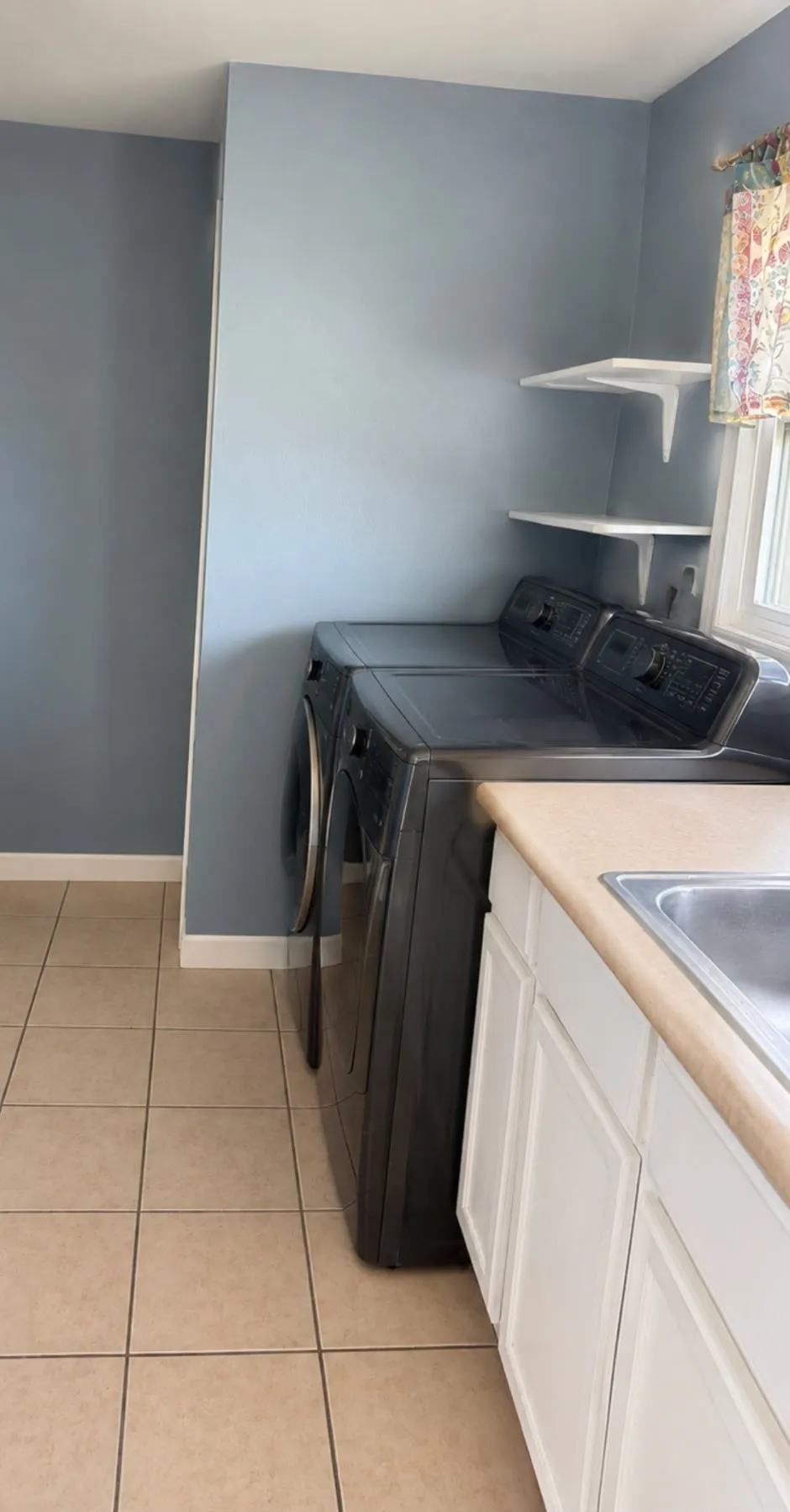 Tile flooring, white cabinetry, light-toned countertop, and floating wall shelves