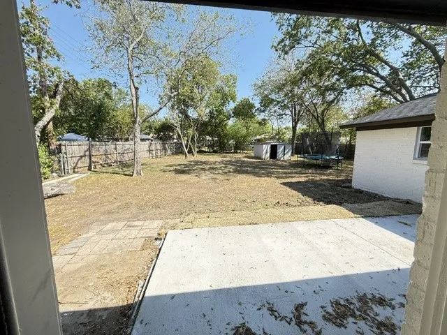 Expansive backyard with a concrete patio, mature trees, and a wood privacy fence