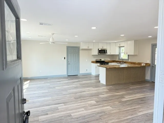 Open-concept living space featuring wood-finish flooring, recessed lighting, a modern ceiling fan, and a kitchen with white cabinetry and a breakfast bar