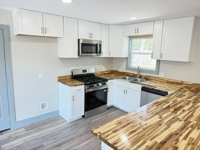 Kitchen featuring wood-finish countertops, white cabinetry, stainless steel appliances, and wood-finish flooring