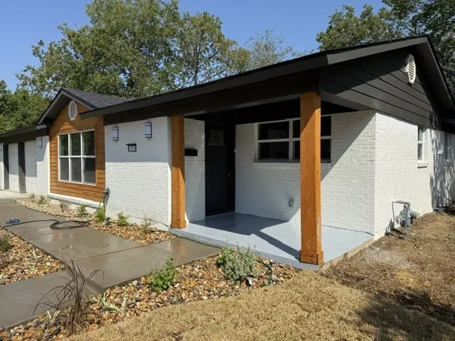 Painted brick exterior with natural wood accents, covered porch with wood posts, and a concrete pathway