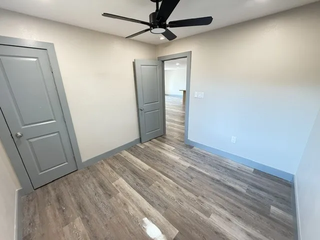 Wood-finish flooring, neutral wall paint, ceiling fan, and paneled doors with contrasting trim