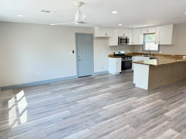 Wood-finish flooring, recessed lighting, white kitchen cabinetry, stainless steel appliances, and a natural stone countertop