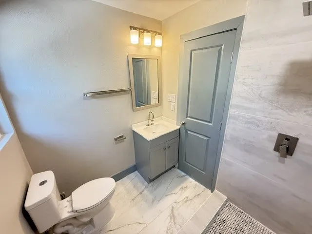 White marble-look flooring, single vanity with a white countertop, chrome faucet, and a shower with large format tile