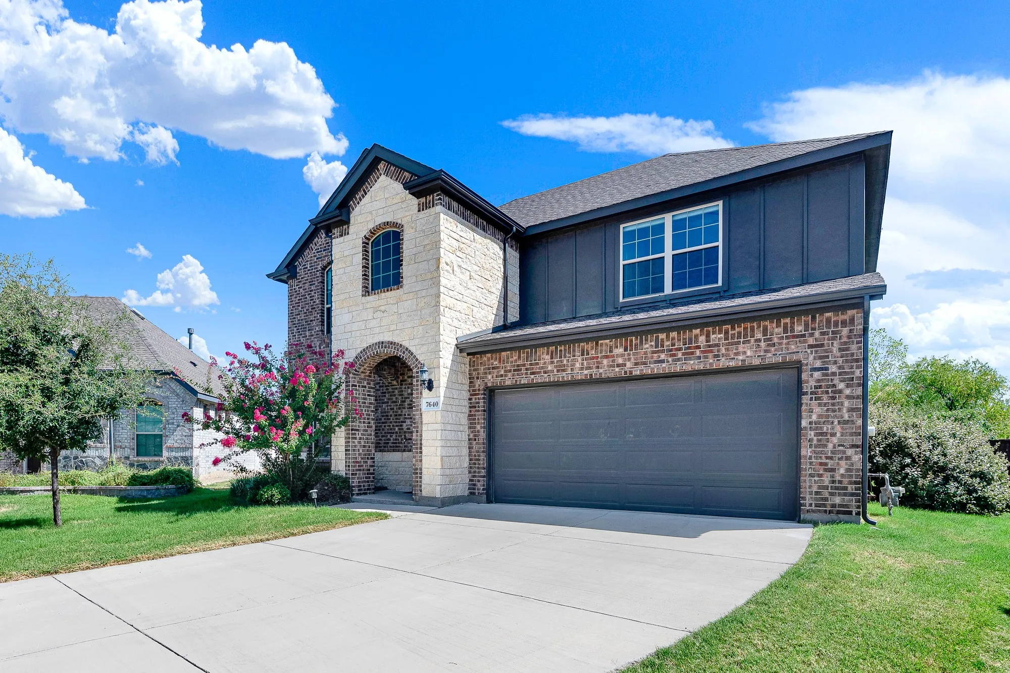 Two-story residence featuring a cream and brick exterior with a peaked gable roofline and dark architectural accents