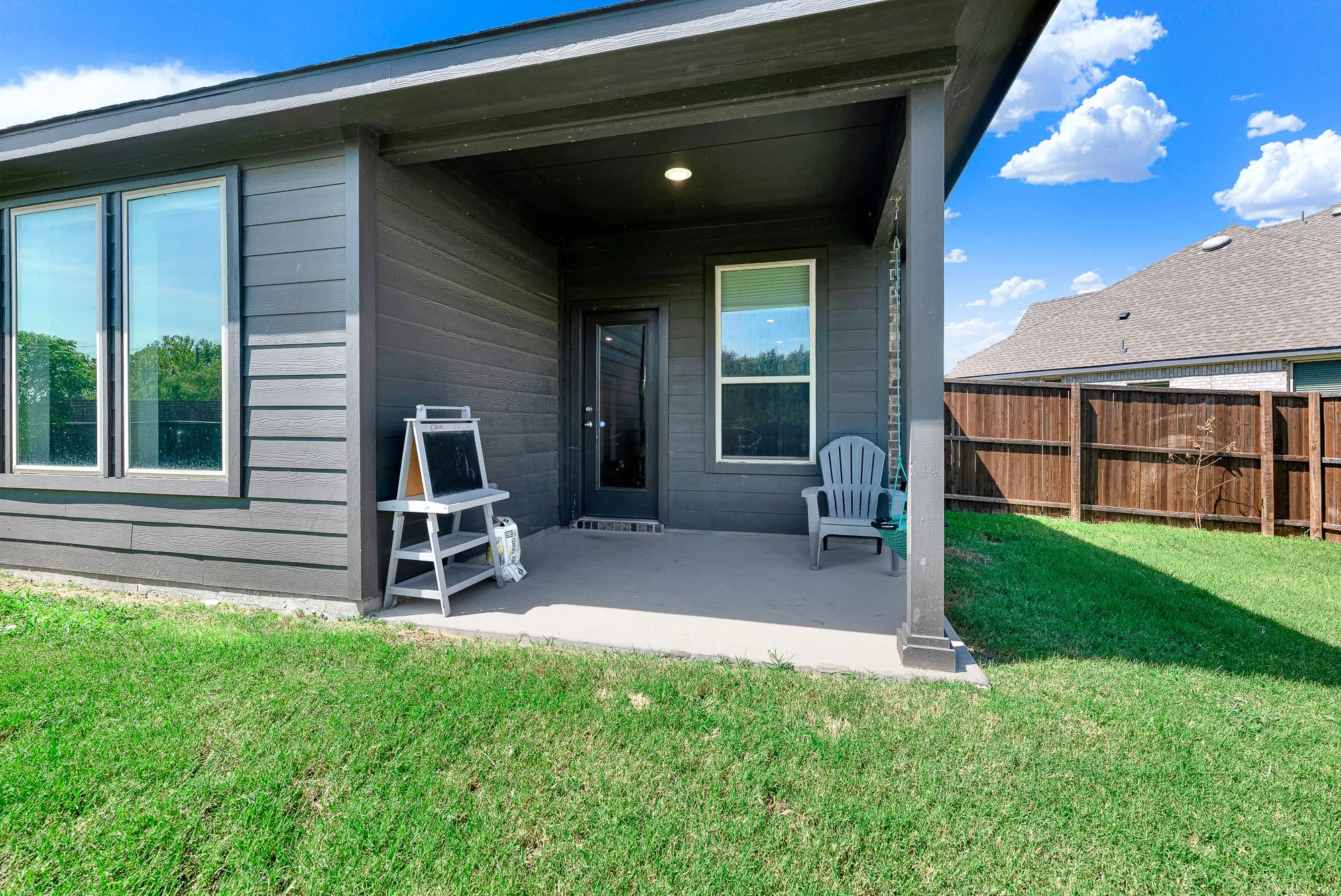 Modern covered patio with concrete flooring and overhead lighting, opening to a manicured lawn