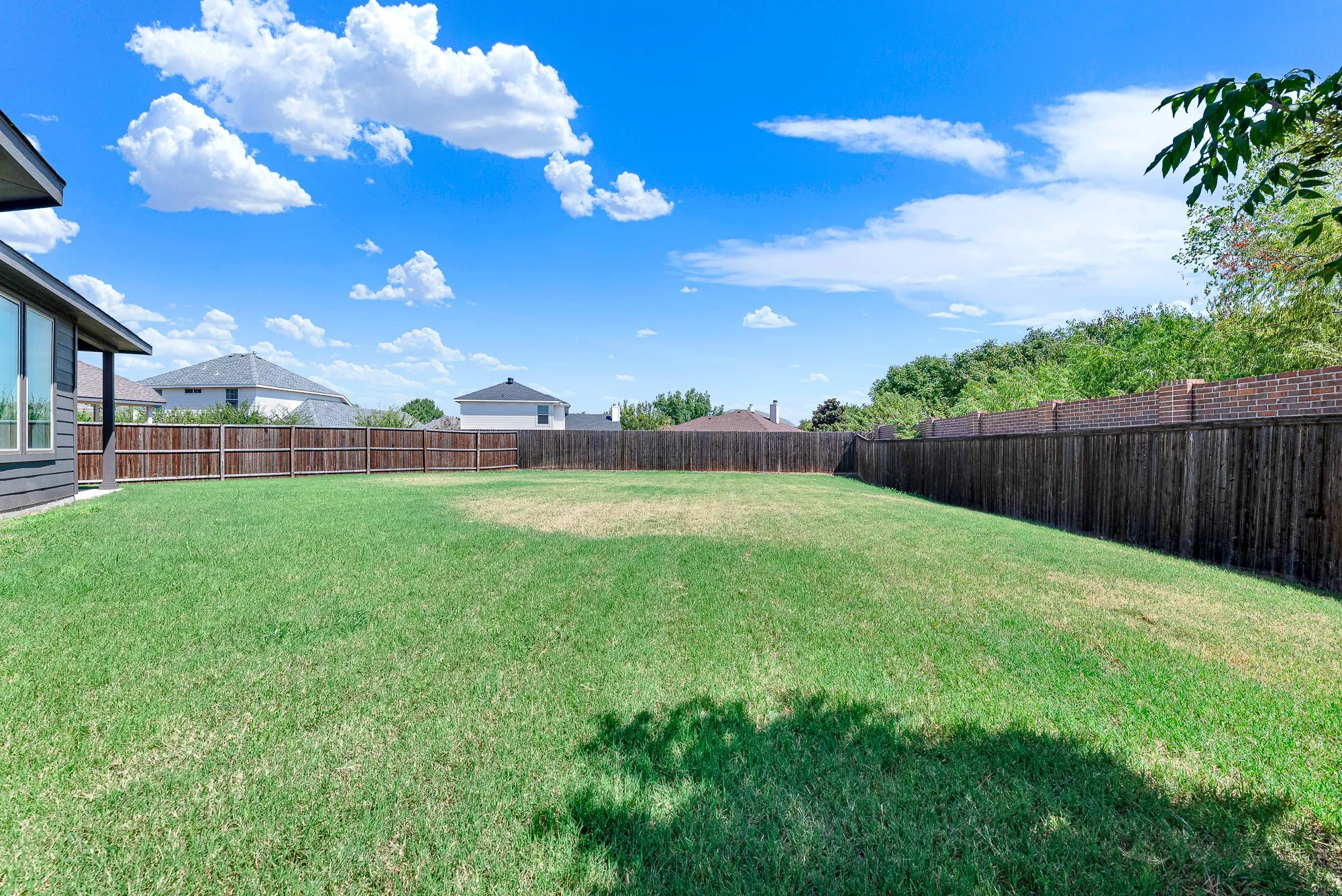 Expansive backyard featuring a generous manicured lawn bordered by dark wood-finish fencing