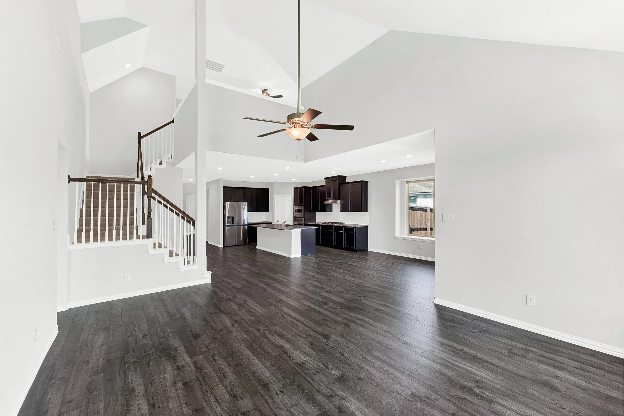 Open-concept living space showcasing soaring vaulted ceilings with skylights, dark wood-finish flooring throughout, and a ceiling fan with integrated lighting