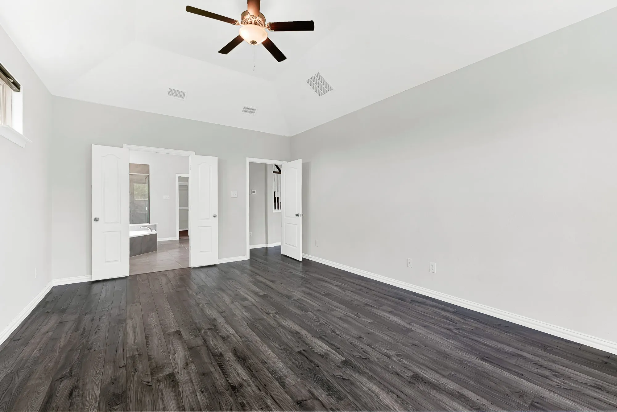 Spacious primary room showcasing dark wood-finish flooring, ceiling fan with brushed metal finish, recessed lighting, and dual French doors with frosted glass panels providing access to adjacent spaces