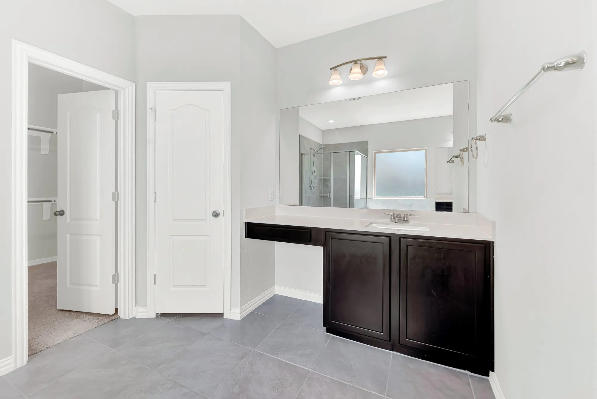 Spa-inspired primary bathroom featuring a dark wood dual-vanity with white quartz countertop, polished chrome fixtures, and large framed mirror with integrated lighting