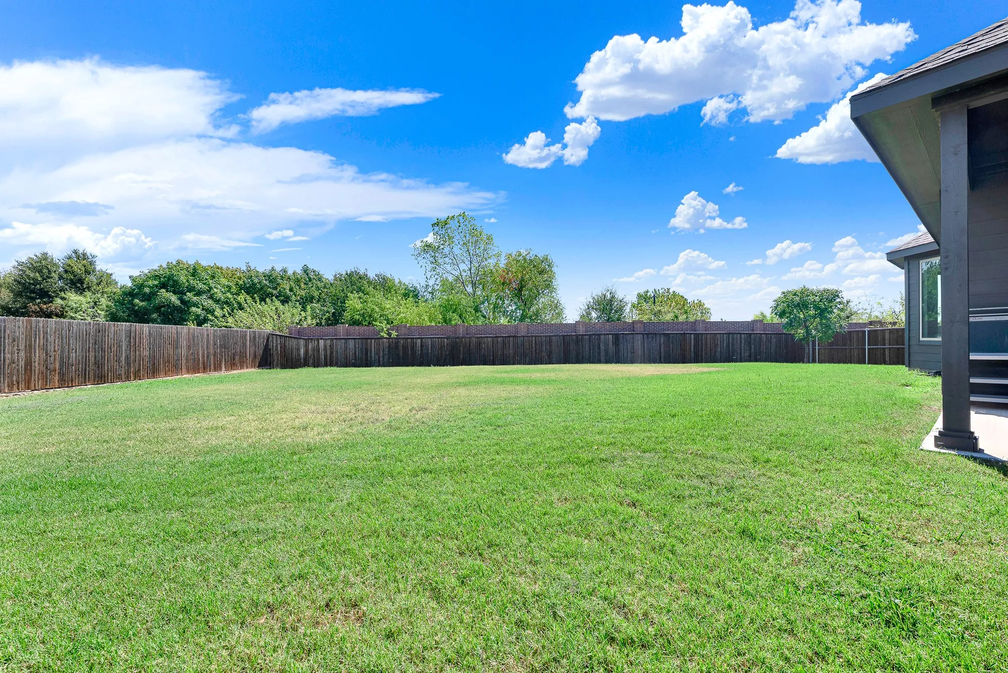 Expansive backyard featuring a meticulously manicured lawn, mature tree line, and wooden privacy fencing
