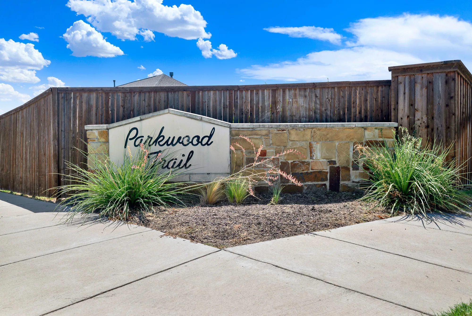 Parkwood Trail community entrance featuring a decorative stone and wood-constructed monument sign with landscaped planting beds and drought-resistant ornamental grasses flanking the base