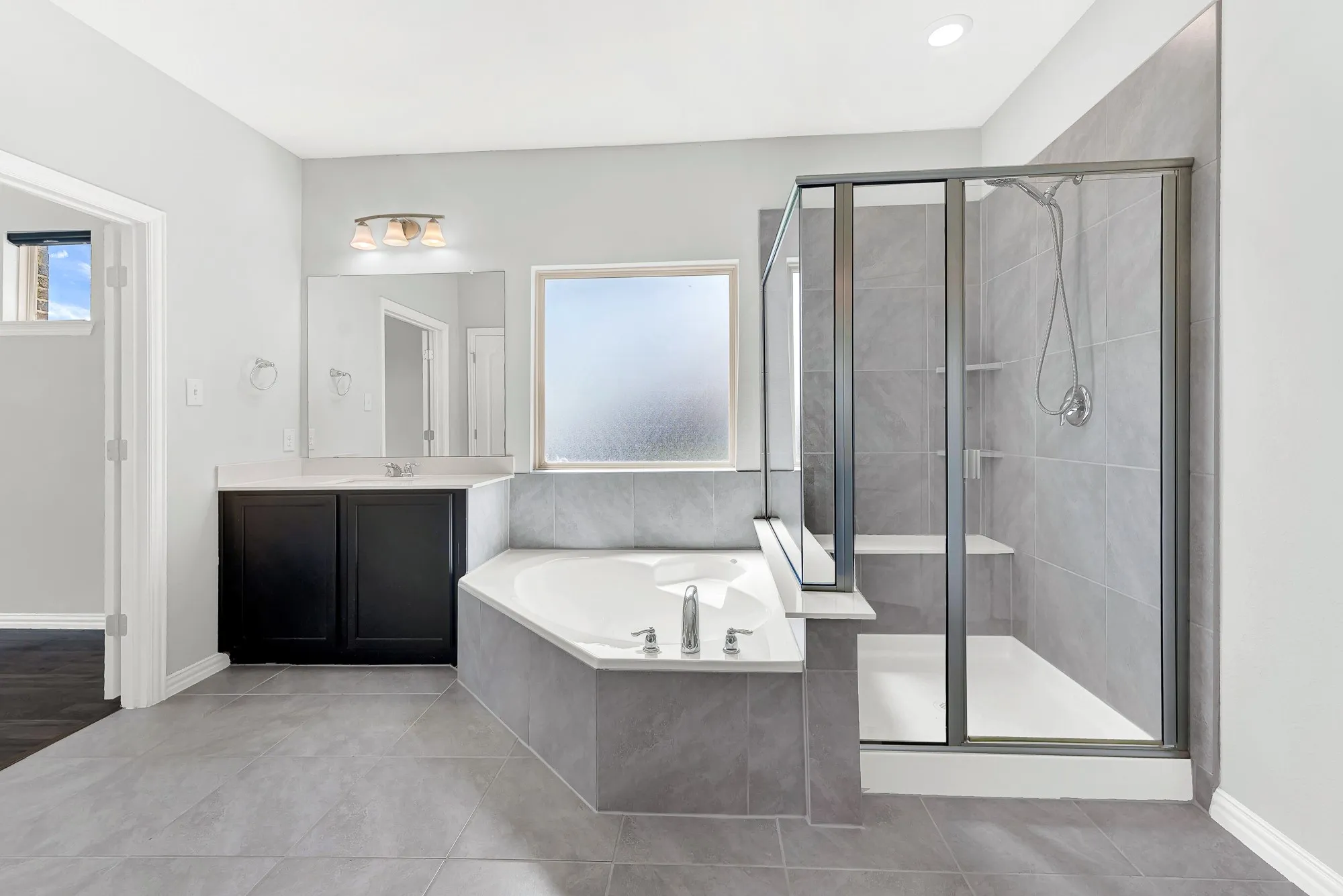 Spa-inspired primary bathroom featuring a freestanding soaking tub with integrated deck, frameless glass-enclosed shower with tile surround, dual vanity with vessel sinks, polished concrete flooring, and abundant natural light from oversized window