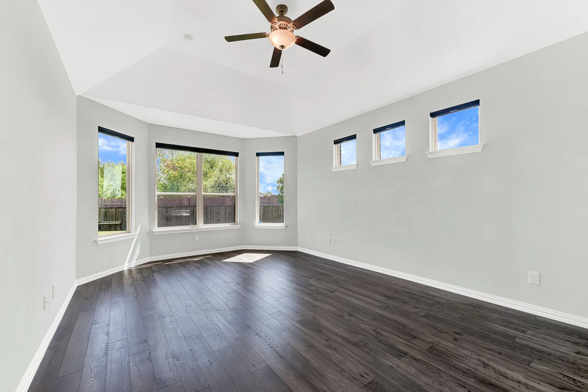 Vaulted ceilings with a ceiling fan, dark wood-finish flooring, a bay window with multiple panes, and additional high windows