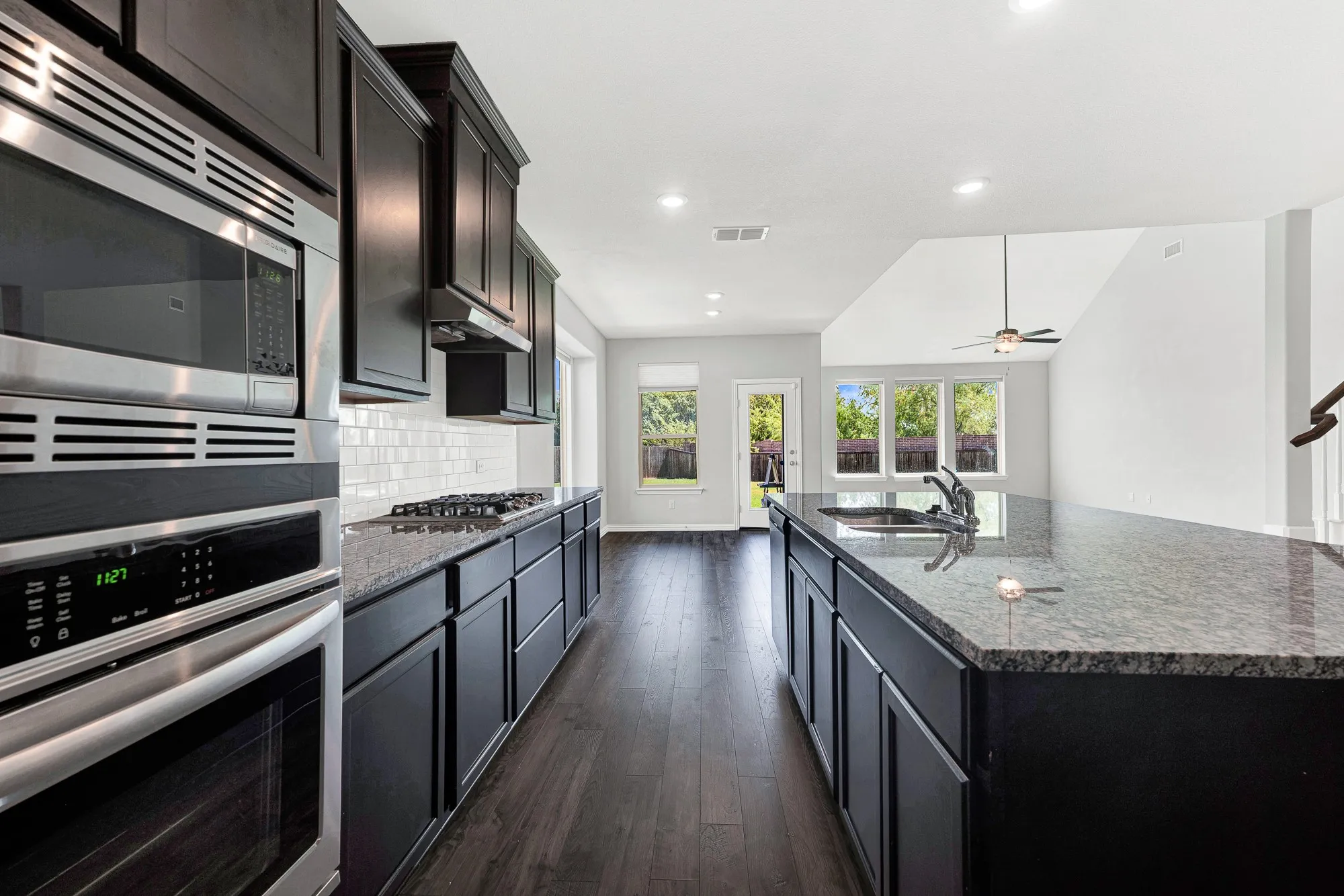 Chef's kitchen featuring dark cabinetry with brushed metal hardware, stainless steel built-in appliances including dual wall ovens and gas cooktop, white subway tile backsplash, and light-colored stone countertops