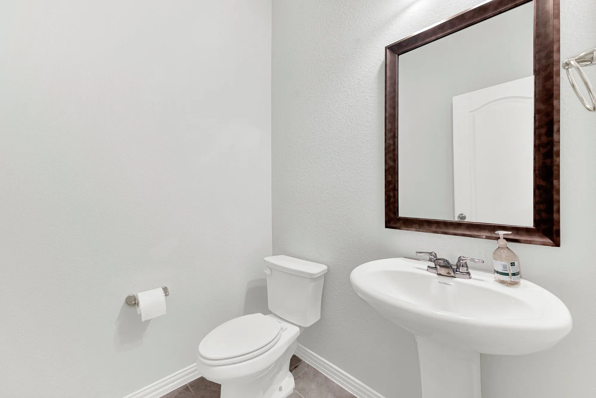 Elegant powder room featuring a pedestal sink with chrome faucet, white porcelain toilet, and a wood-framed mirror above marble countertops