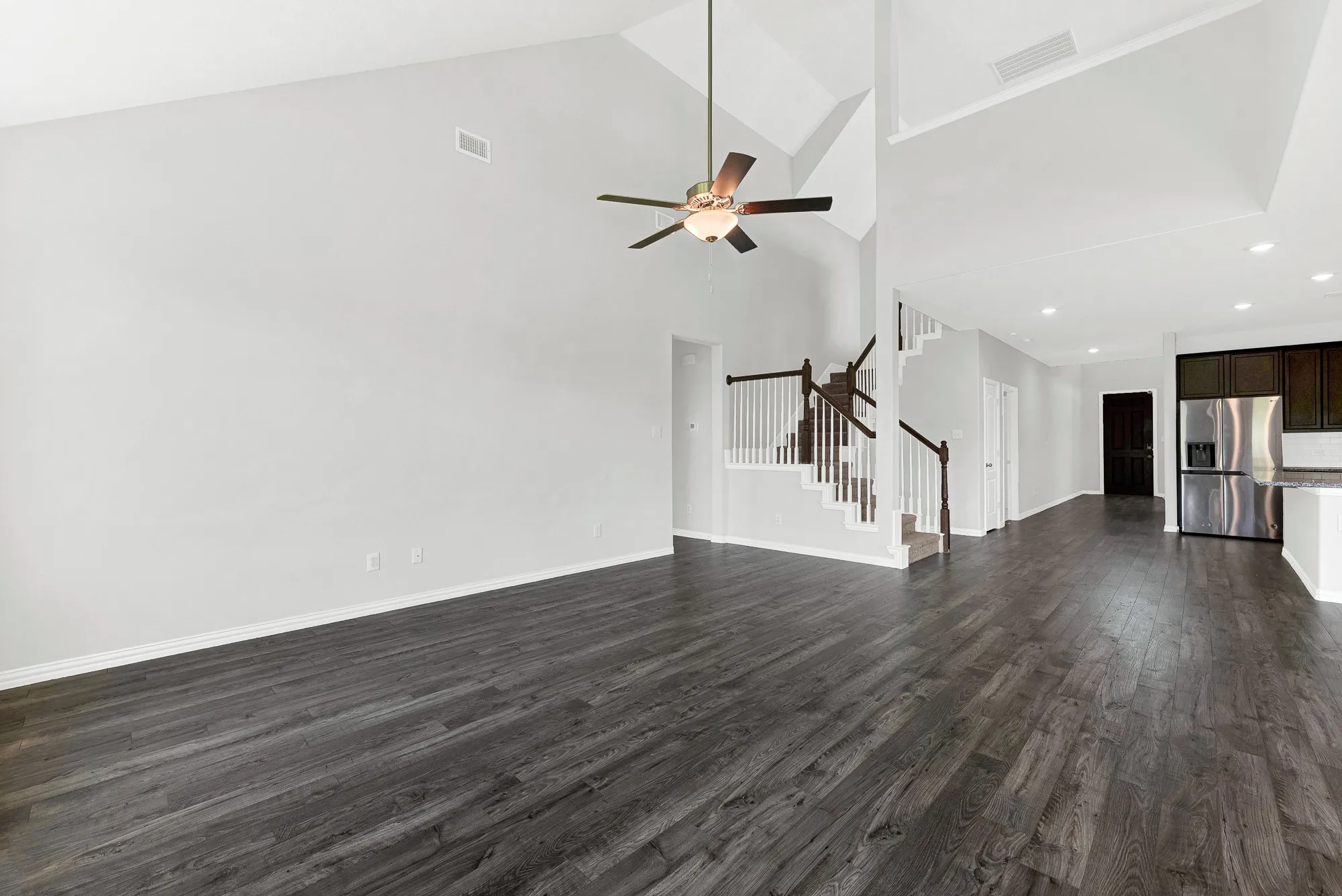 Vaulted ceilings, wood-finish flooring, staircase with white spindles, dark wood cabinetry, and stainless steel refrigerator