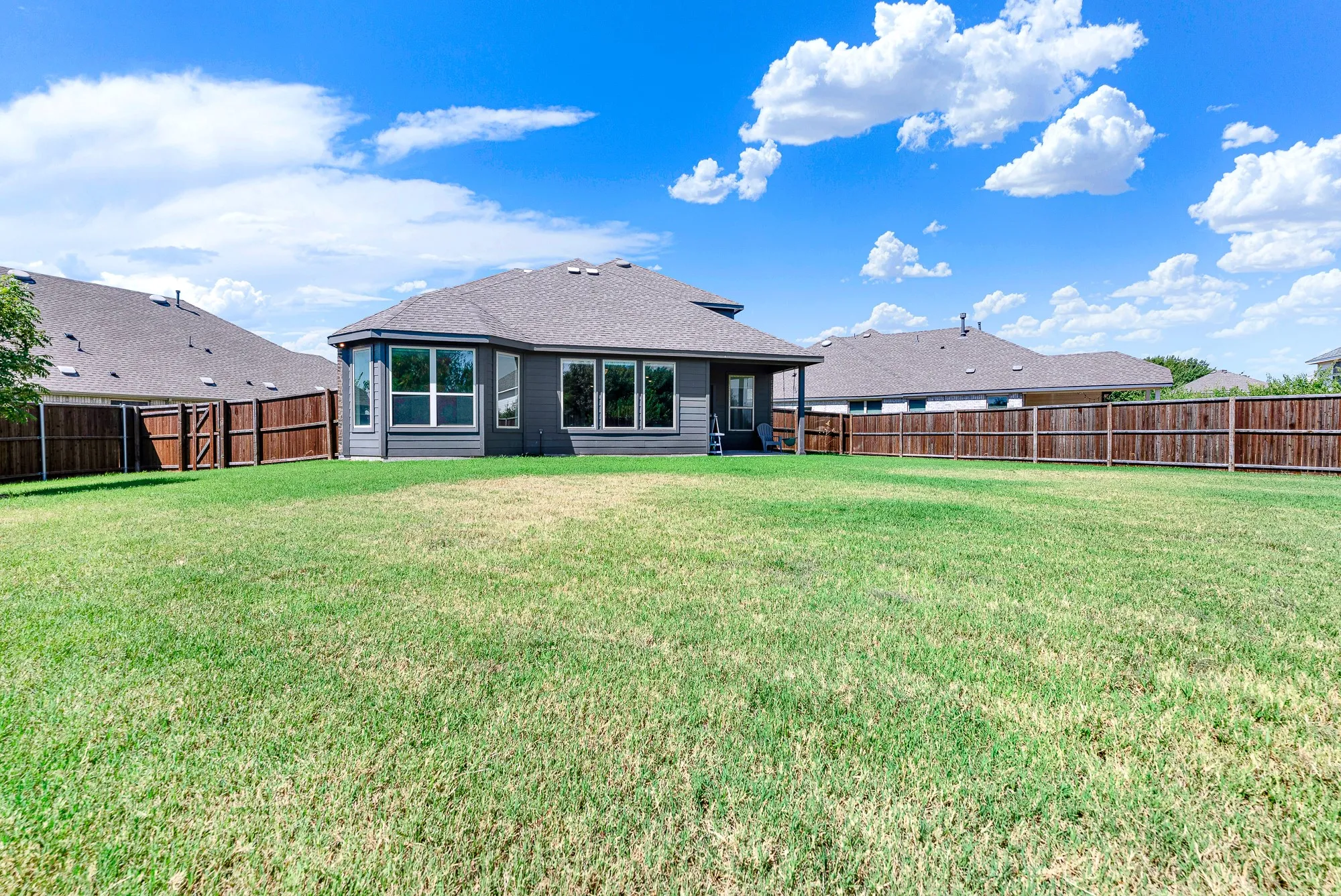 Expansive backyard featuring a manicured lawn with mature landscaping and wood-finish fencing