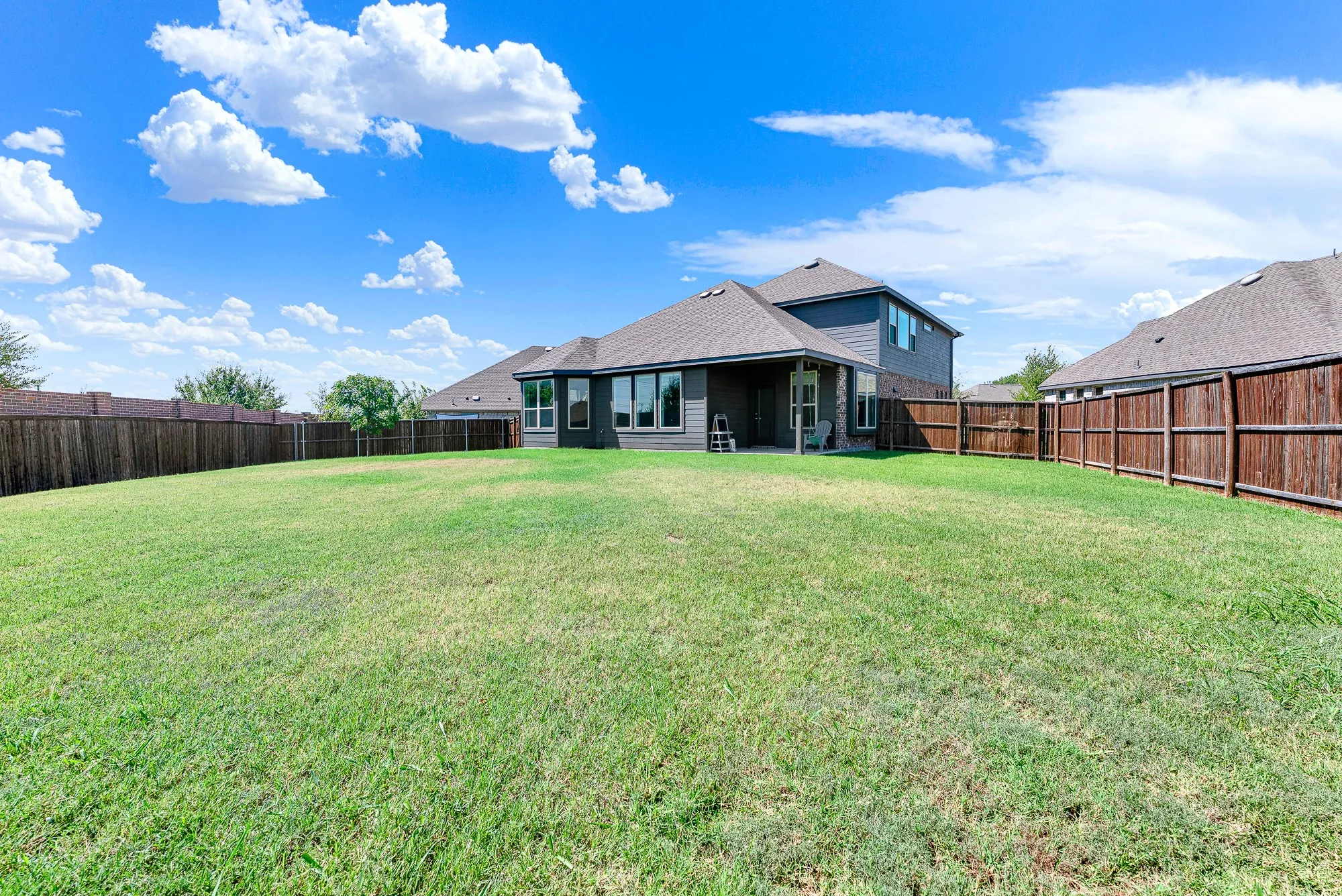 Expansive backyard with a manicured lawn, full privacy fencing, and a covered patio area