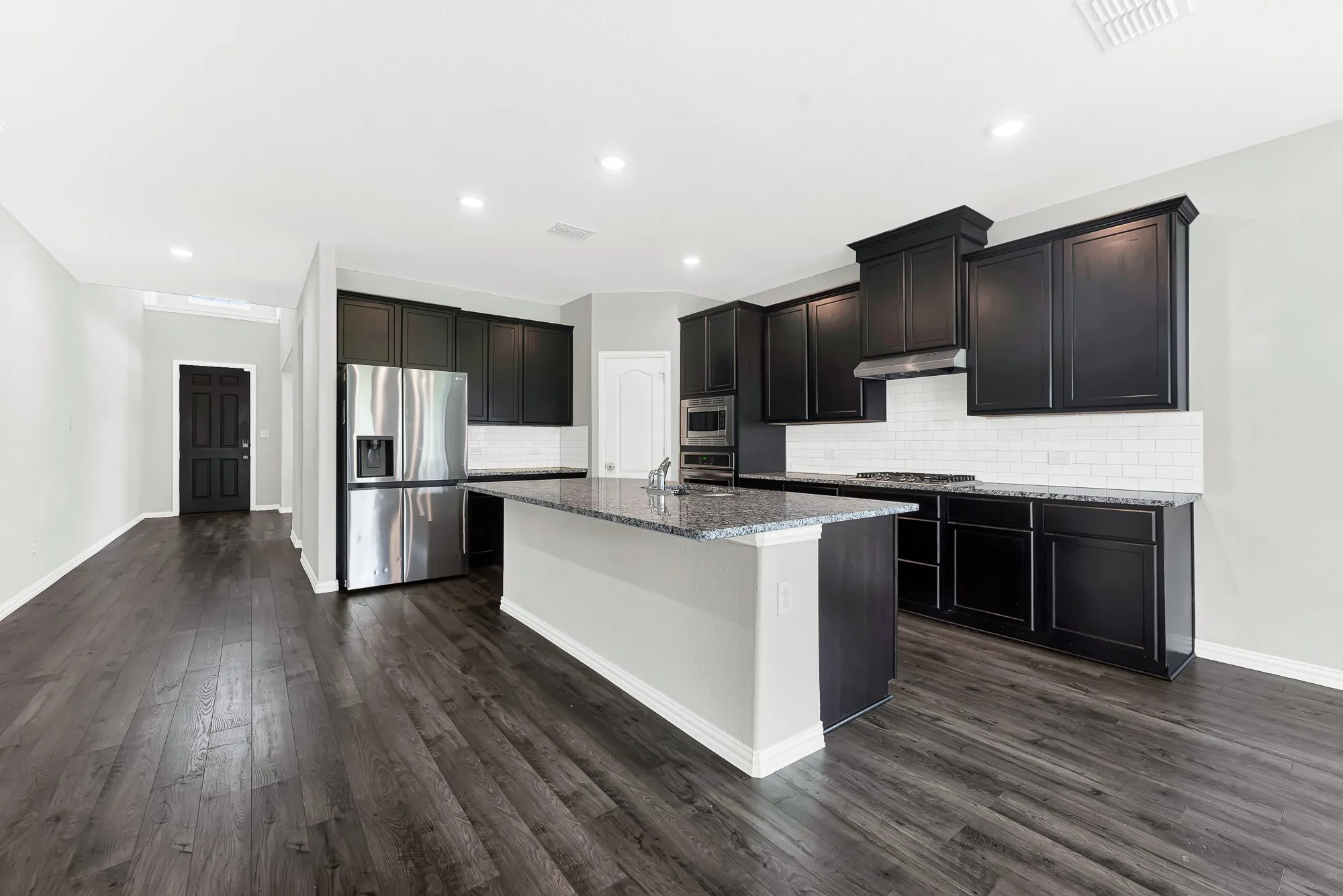 Spacious kitchen with a central island, dark wood-finish flooring, and black cabinetry