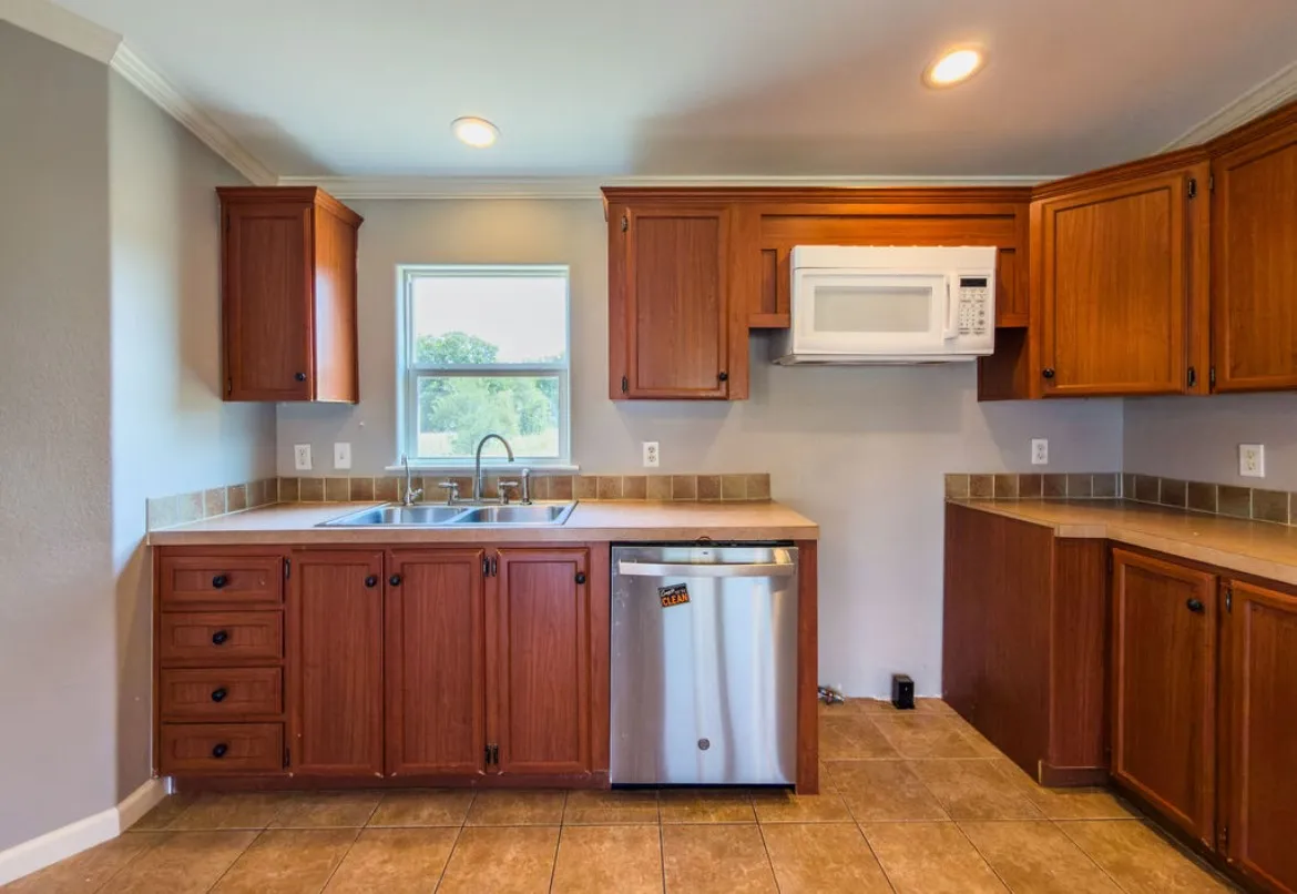 Kitchen featuring wood-finish cabinetry, stainless steel dishwasher, double basin sink, neutral countertops, and tile flooring