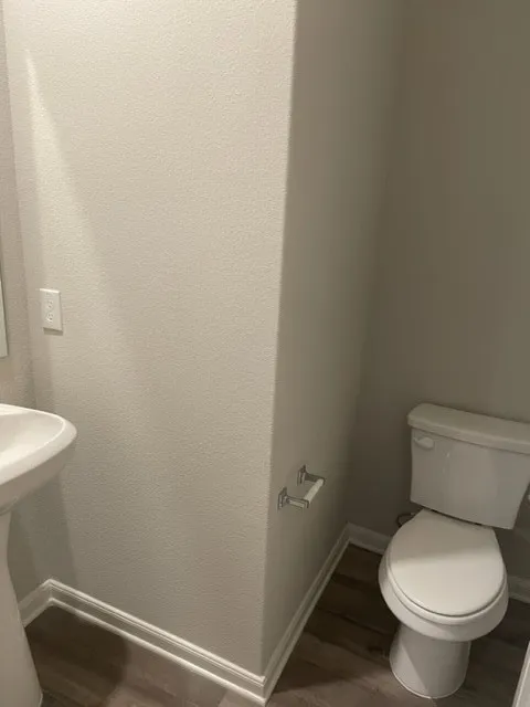 Pedestal sink with wood-finish flooring, white trim, and a wall-mounted toilet paper holder