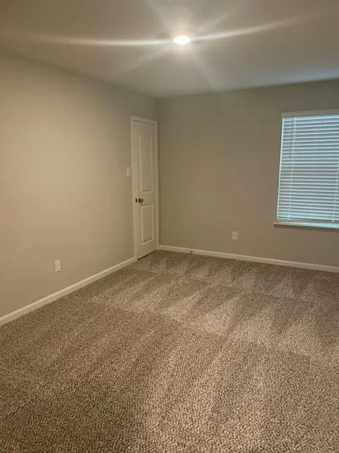 Recessed ceiling lighting, neutral wall paint, white interior door, window with horizontal blinds, and textured carpeting