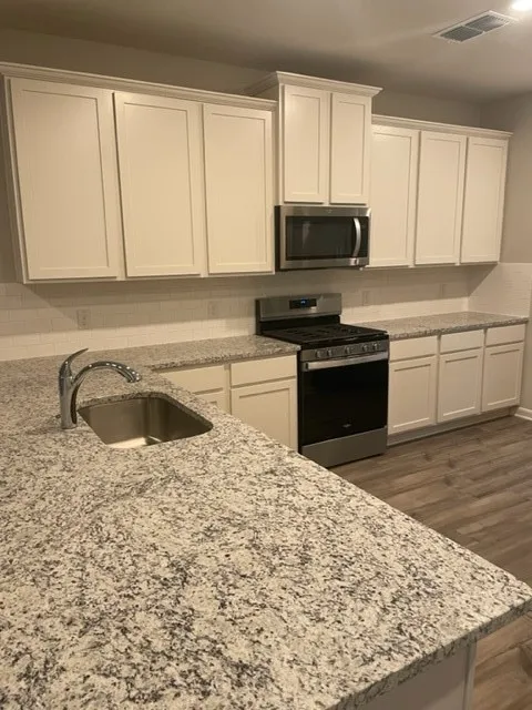 White shaker-style cabinetry, stainless steel appliances, granite countertops, single-basin stainless steel sink, and wood-finish flooring
