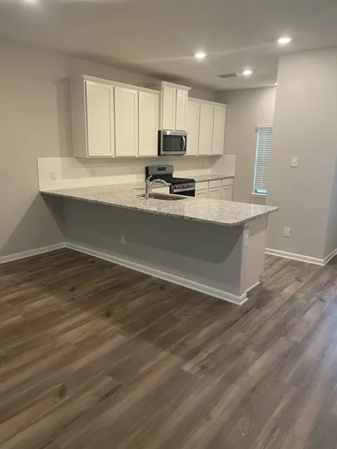 Kitchen featuring wood-finish flooring, white cabinetry, granite countertops, tile backsplash, and stainless steel appliances