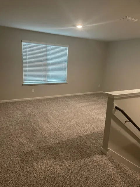 Carpeted room featuring a window with blinds, recessed lighting, and a painted stair railing