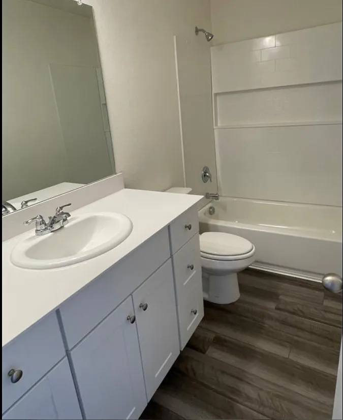 Vanity with an integrated sink and chrome fixtures, white cabinetry with chrome hardware, wood-finish flooring, and a shower-over-tub combination with a subway-tiled surround