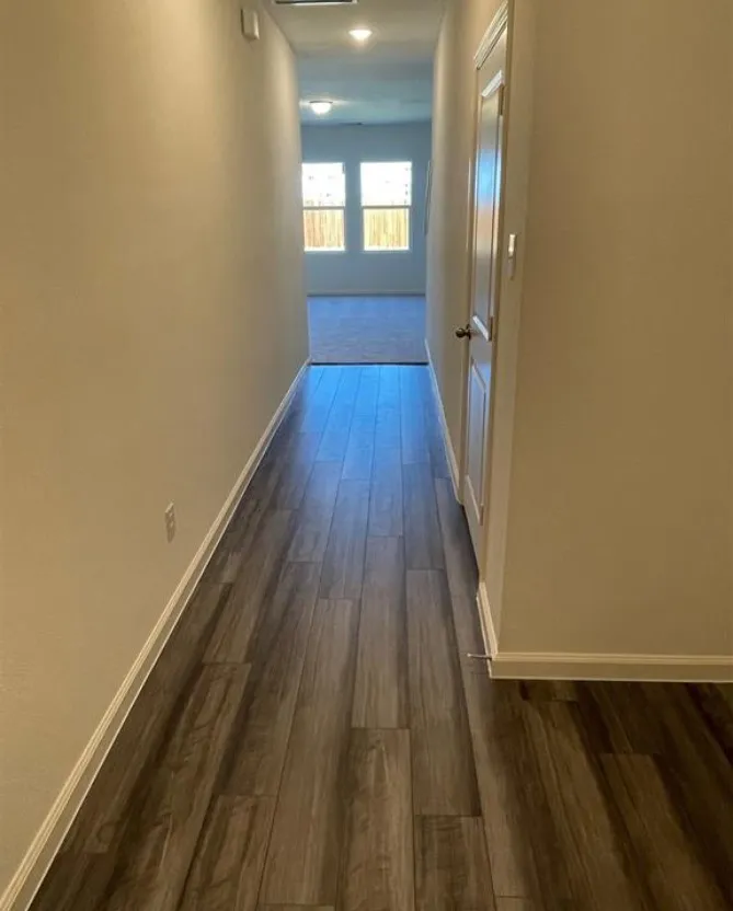 Hallway featuring wood-finish flooring, light neutral wall tones, and white trim