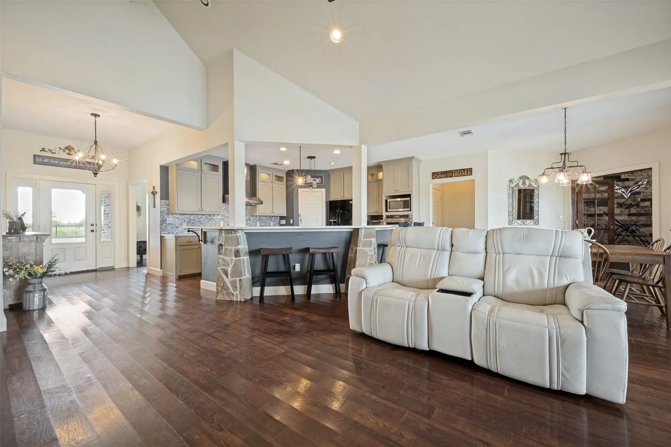 Vaulted ceilings, wood-finish flooring, kitchen with stone-accented breakfast bar, pendant lighting, and recessed lighting