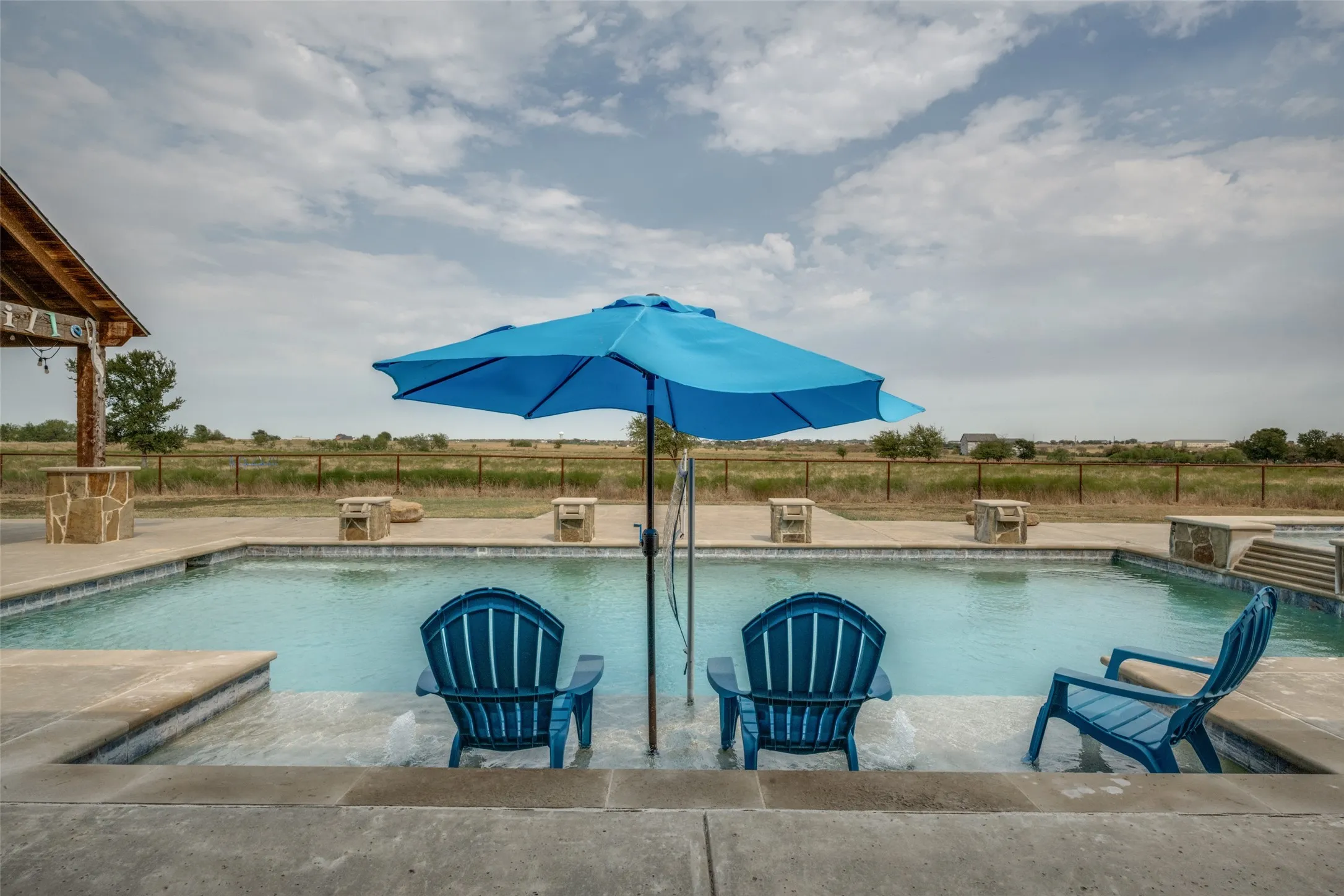 Rectangular inground pool with integrated sun shelf, adjacent spa with stone surround, and expansive concrete decking