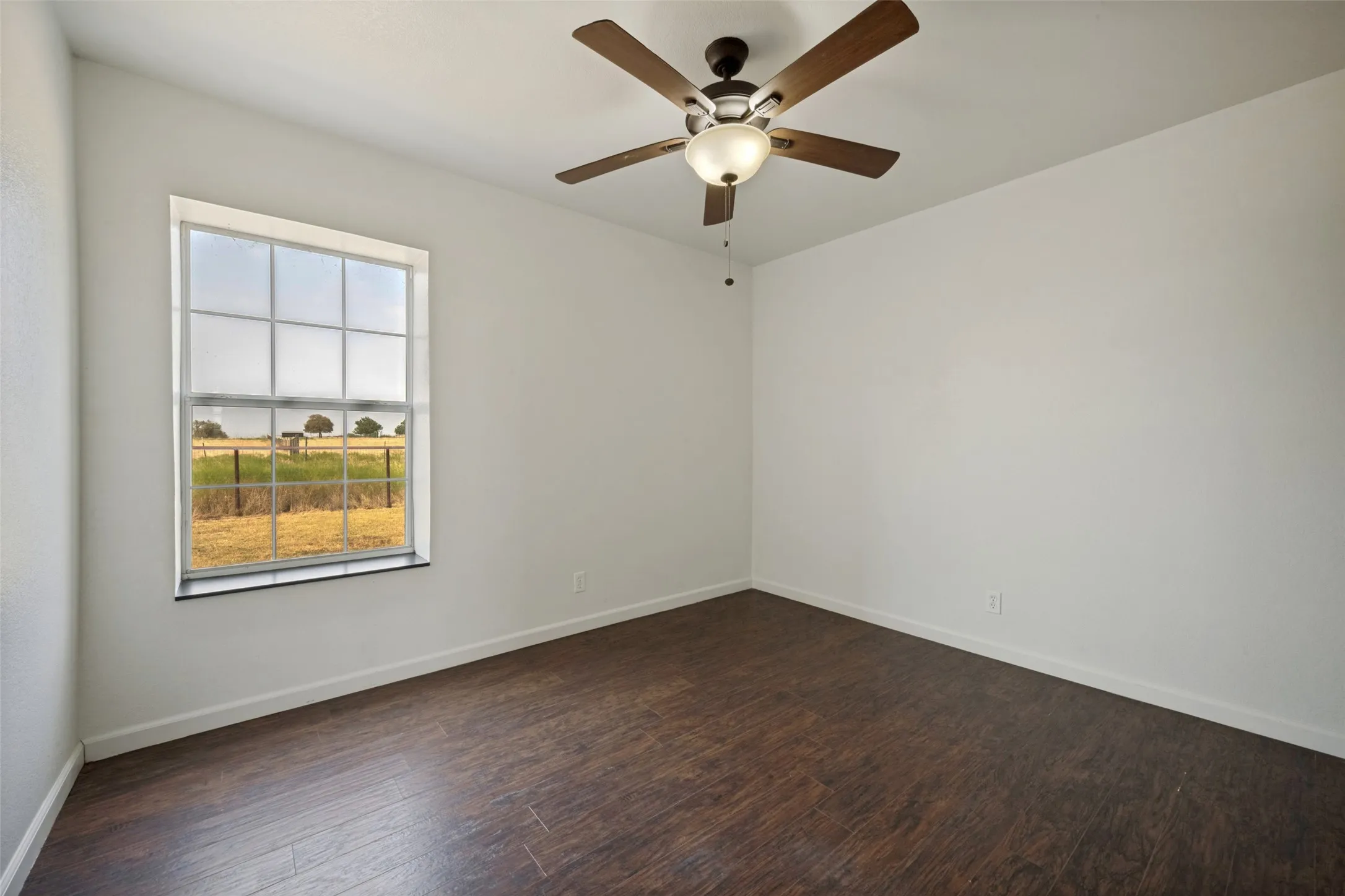 Wood-finish flooring, white painted walls, ceiling fan with integrated lighting, and a multi-pane window