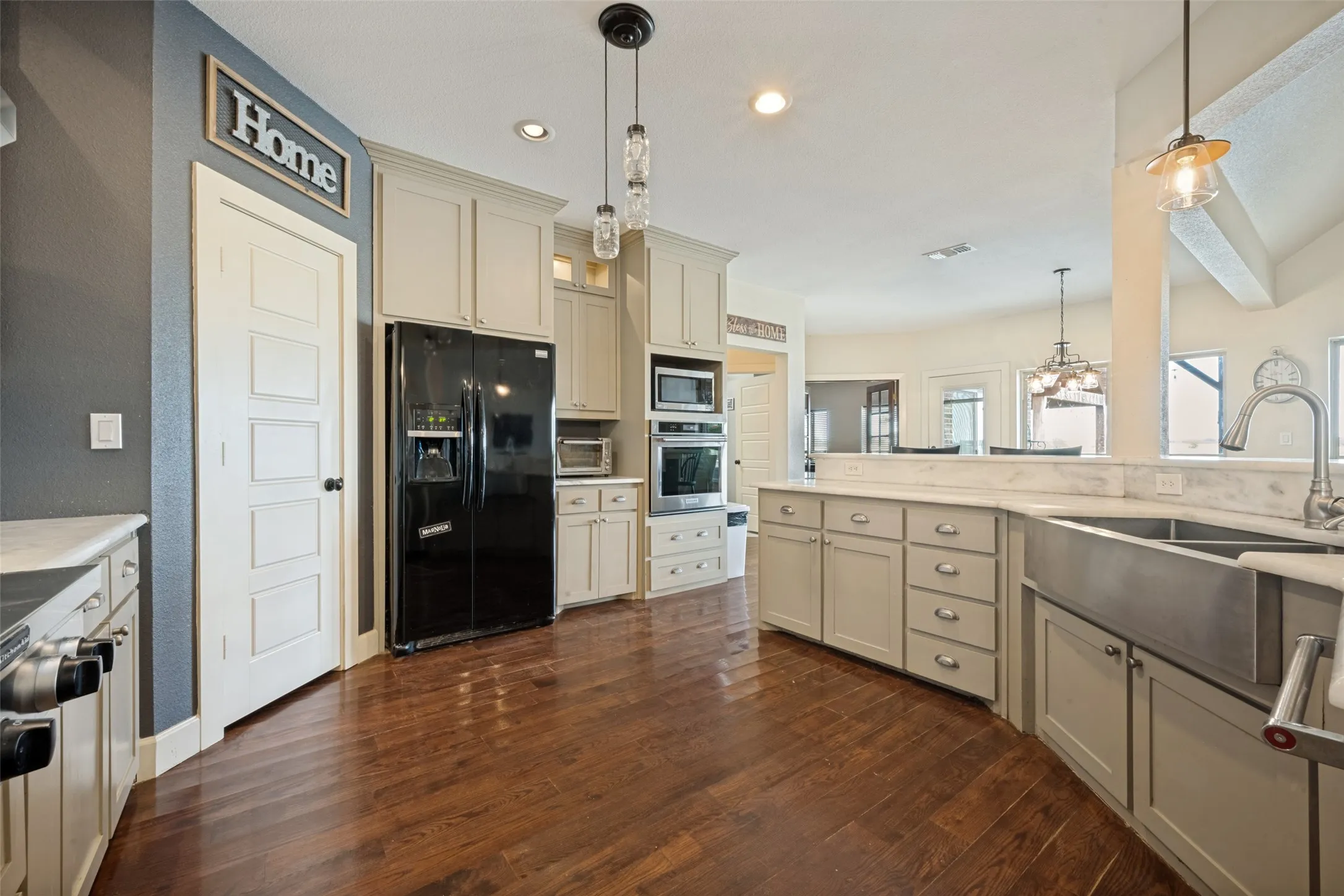 Spacious kitchen featuring cream cabinetry, stainless steel appliances including a double wall oven and side-by-side refrigerator, wood-finish flooring, and a large center island with sink and prep space