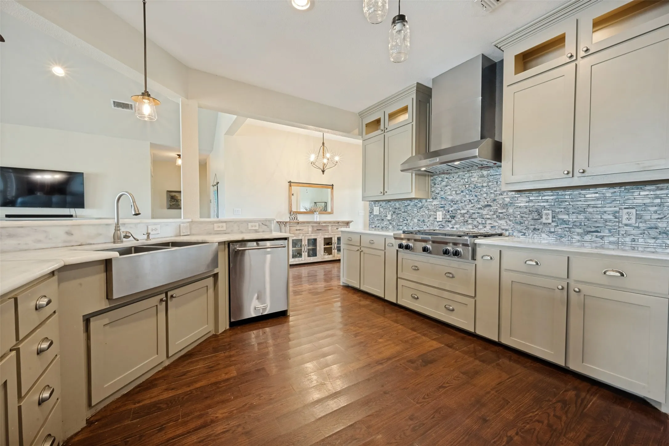 Kitchen featuring hardwood-finish flooring, light-toned cabinetry with pulls, stainless steel appliances, a farmhouse sink, and a mosaic tile backsplash