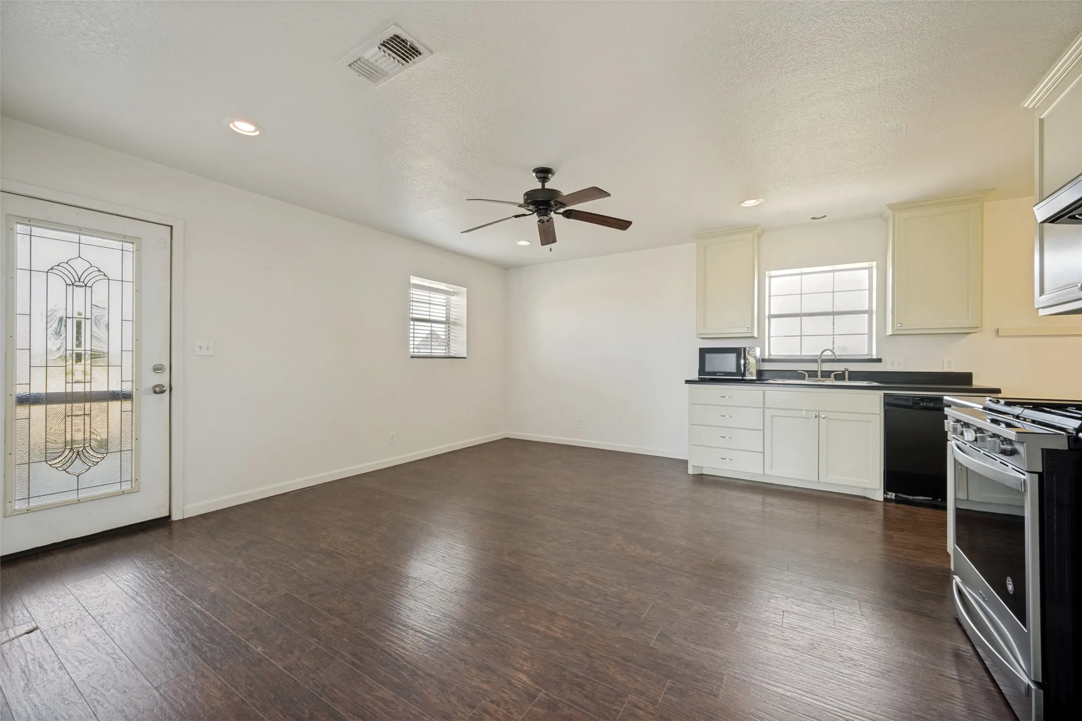 Wood-finish flooring, recessed lighting, ceiling fan, white cabinetry with dark countertops, and stainless steel appliances