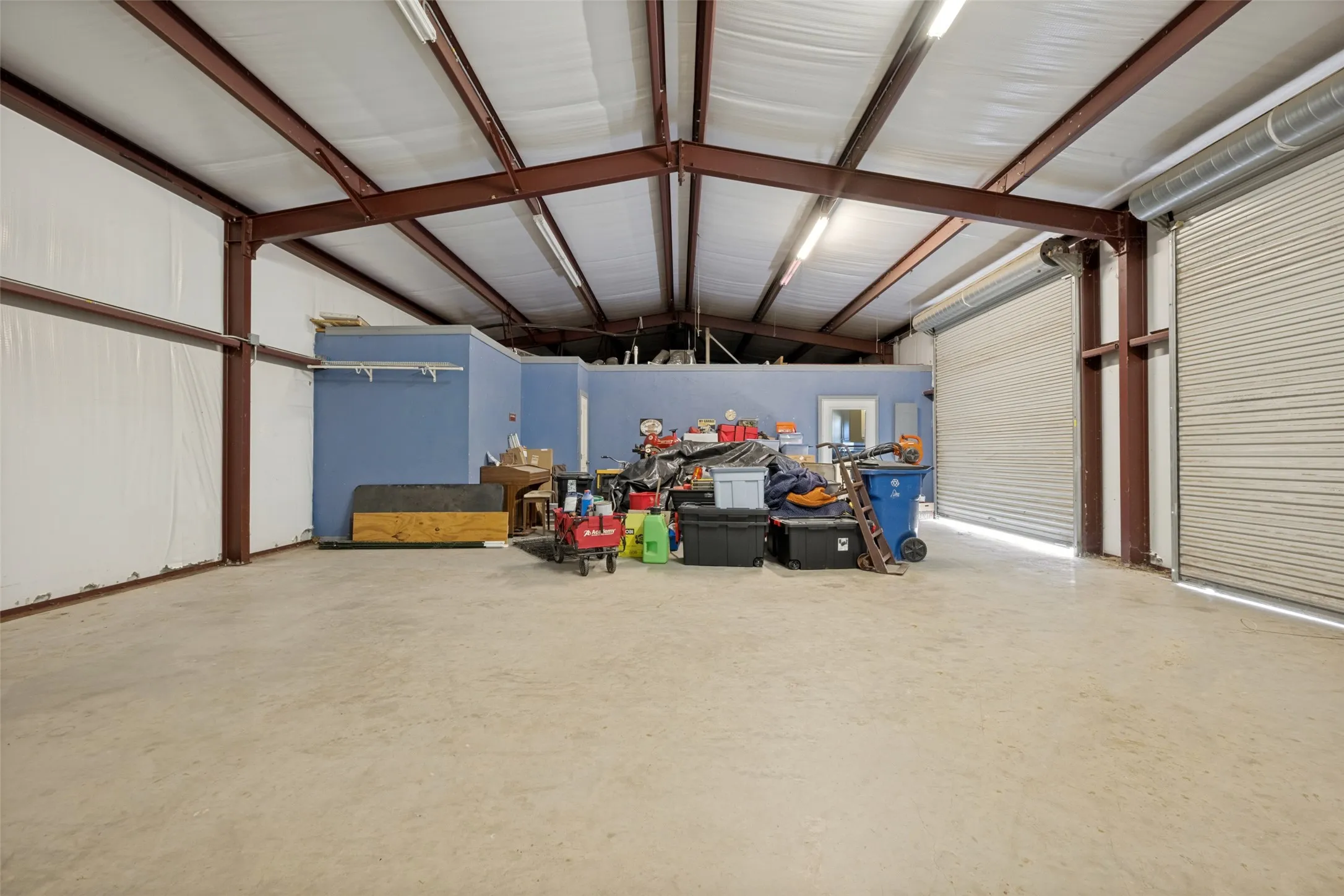 Barndo garage space  interior with exposed steel beam construction, a concrete floor, and two large roll-up doors