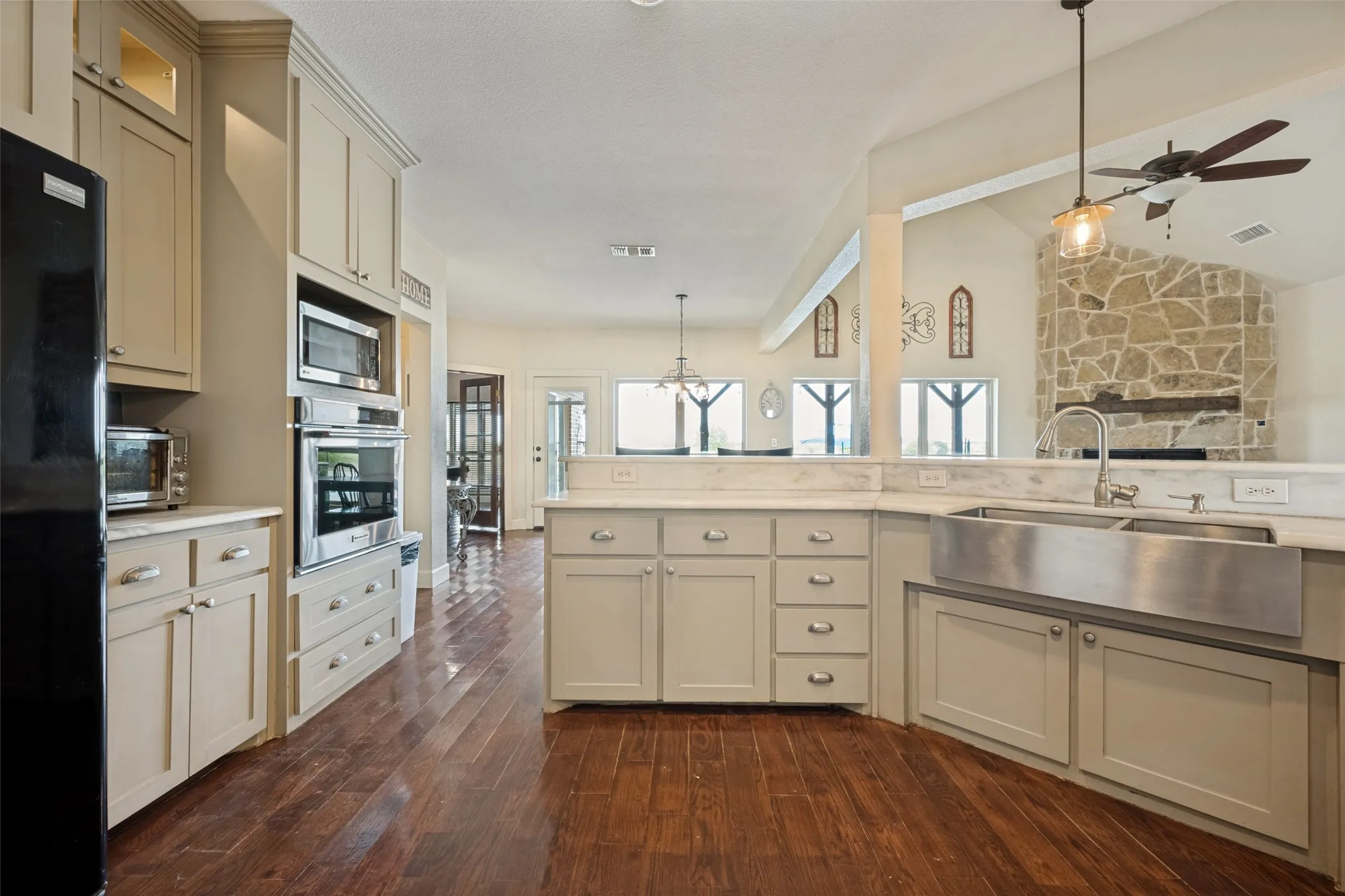 Kitchen featuring wood-finish flooring, light-colored cabinetry, stainless steel appliances, a farmhouse sink, and stone accent wall