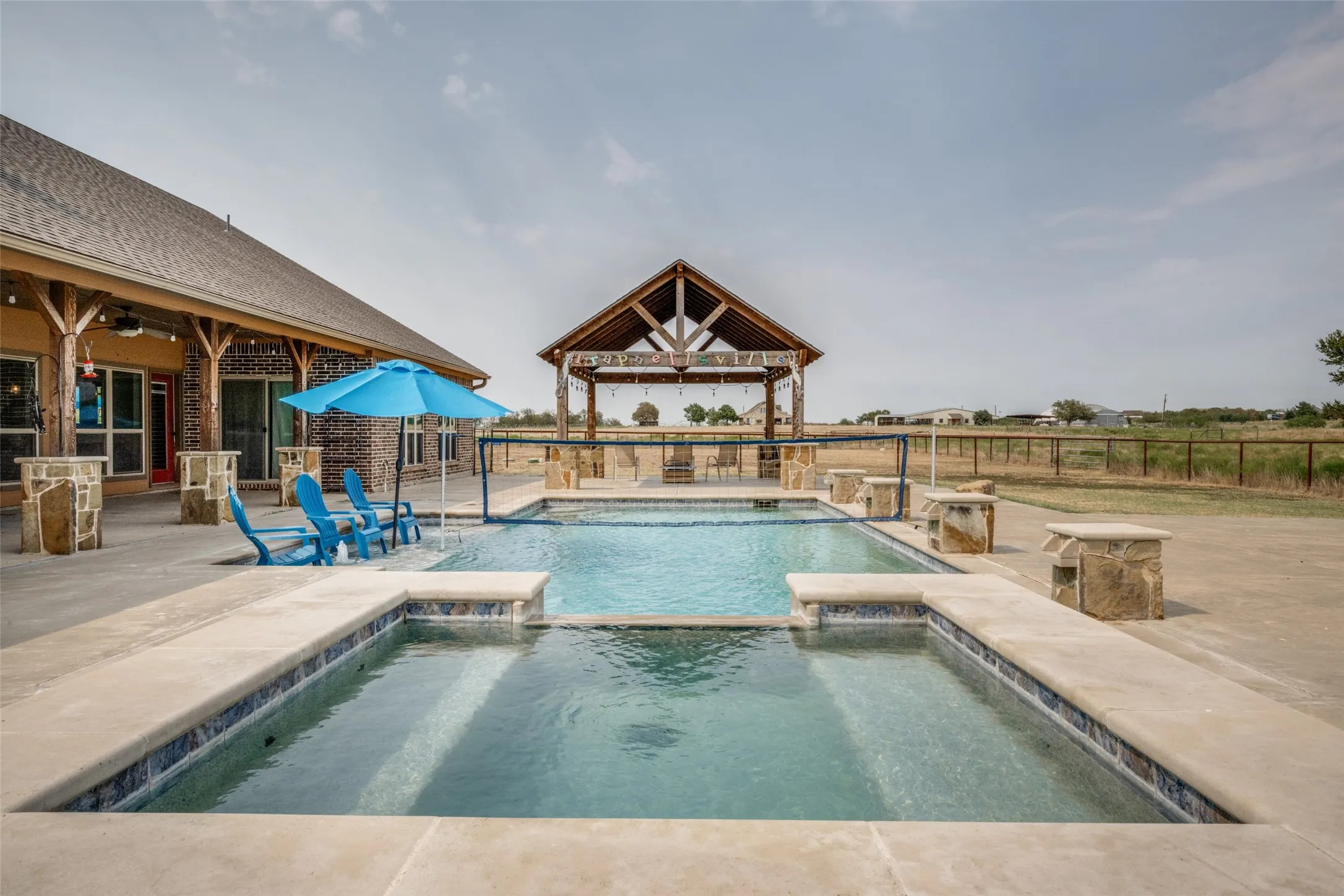 Expansive concrete patio with a built-in swimming pool and spa, featuring stone-clad water features