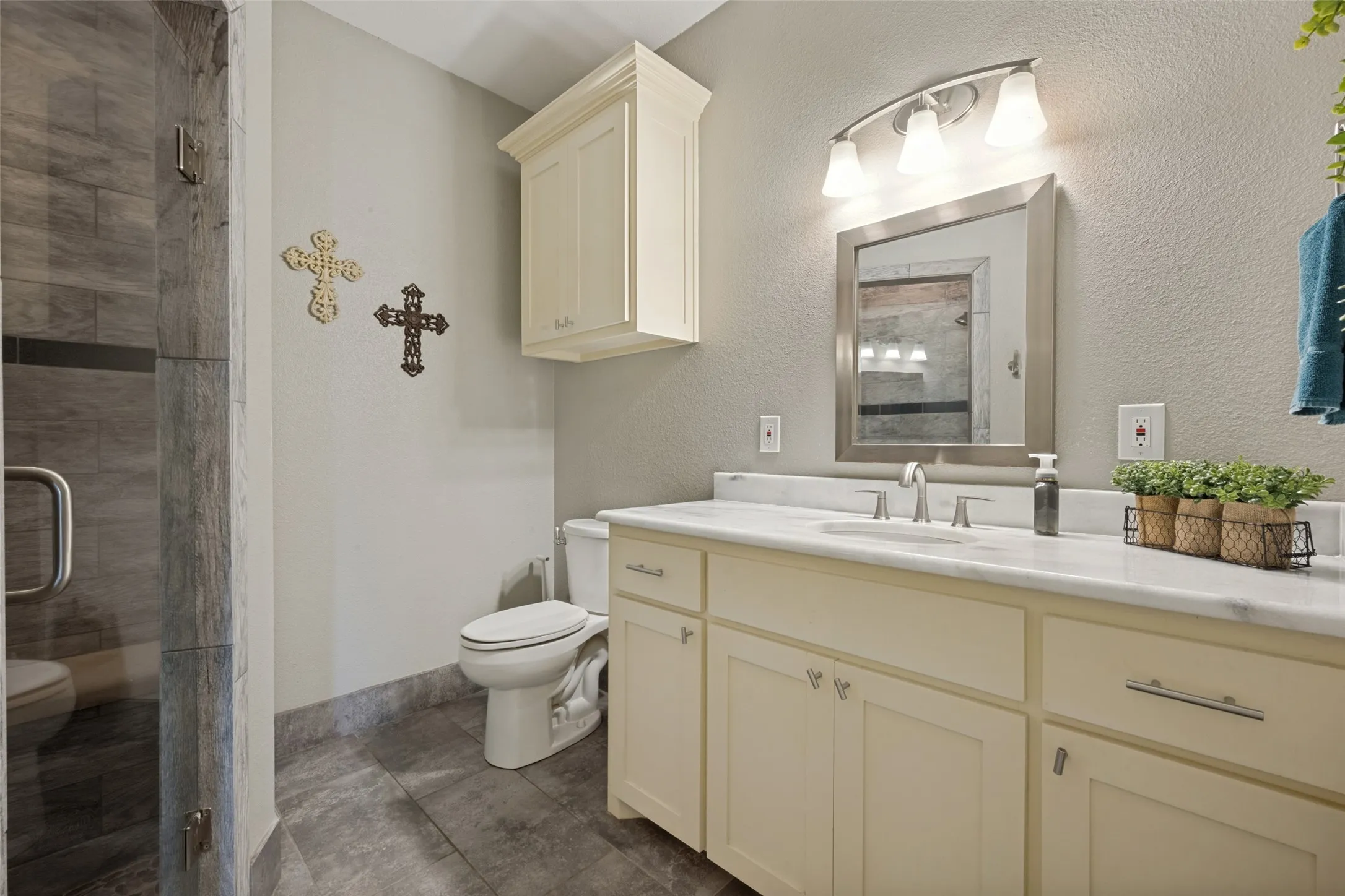 Walk-in shower with tile surround, vanity with light-colored cabinetry, polished countertop, and an integrated sink
