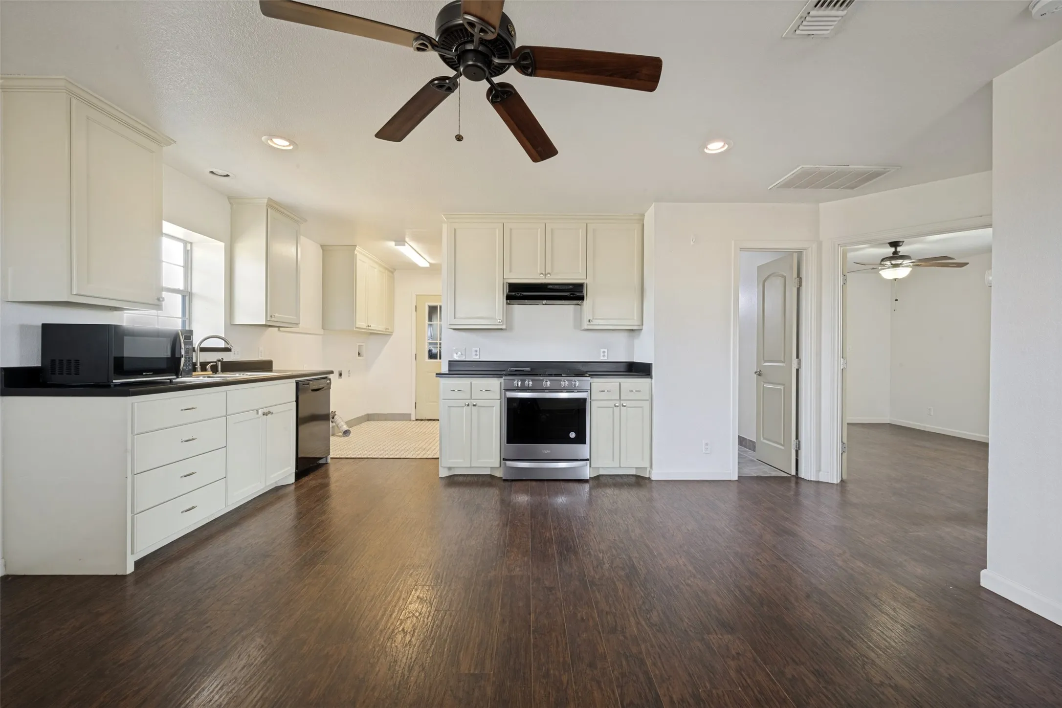Open-concept living space with dark wood-finish flooring, white cabinetry, dark countertops, and stainless steel appliances