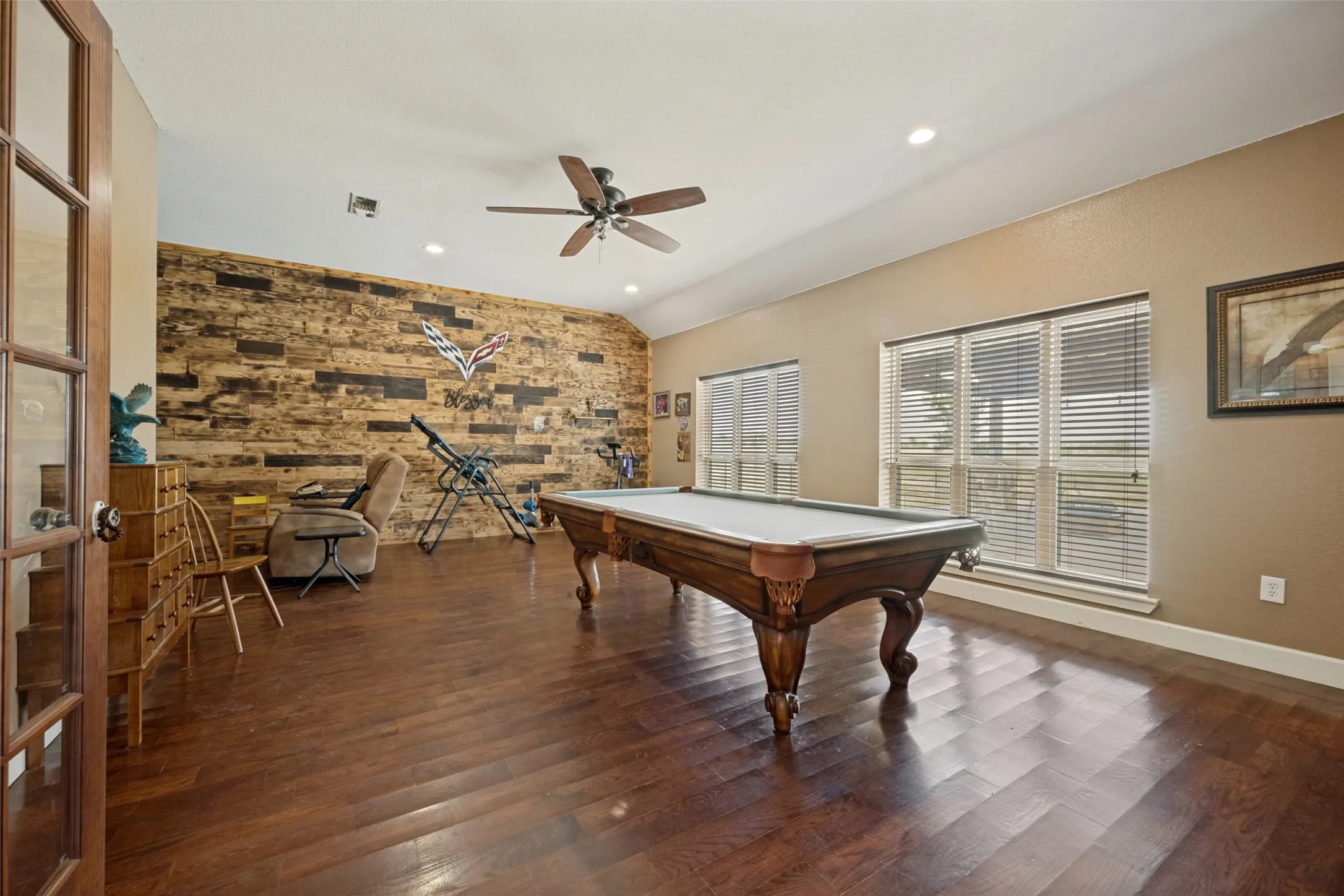 Family room with wood flooring, wood-paneled accent wall, recessed lighting, ceiling fan, and French doors