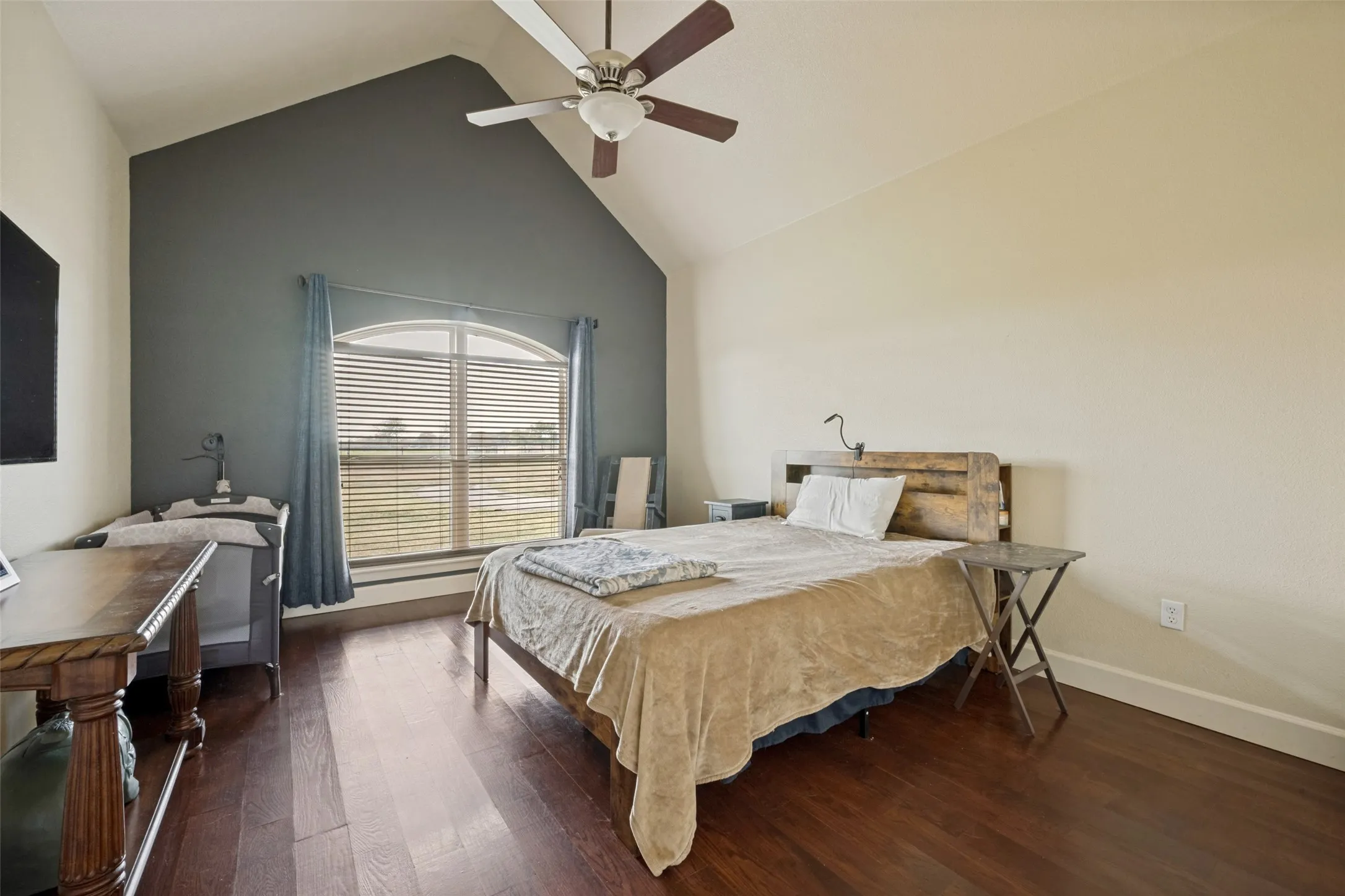 Vaulted ceiling with a ceiling fan, arched window with horizontal blinds, wood-finish flooring, and a contrasting accent wall
