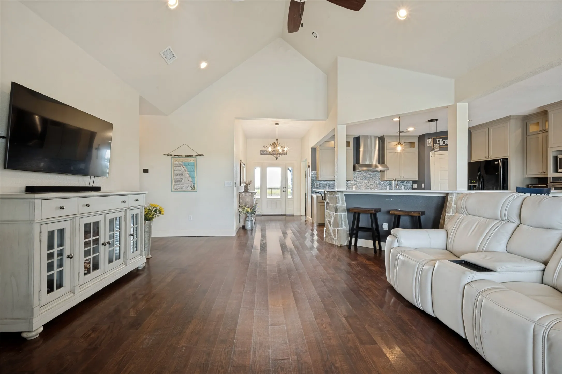 Vaulted ceilings with recessed lighting, wood-finish flooring, kitchen pass-through with stone-clad half wall, stainless steel range hood, and pendant lighting