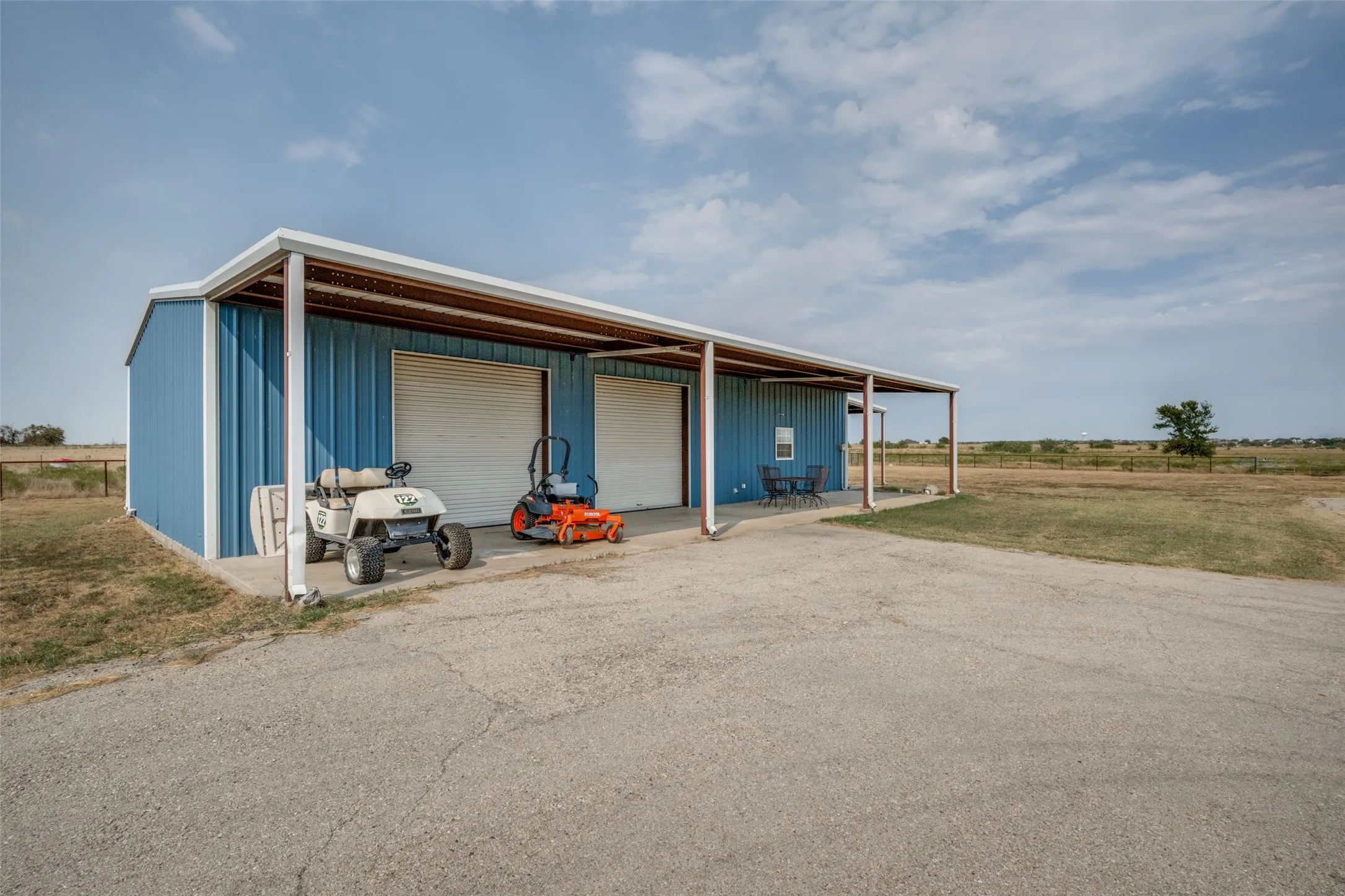 Barndo -Blue metal building with two garage doors, an extended covered porch, a concrete driveway, and an expansive open landscape
