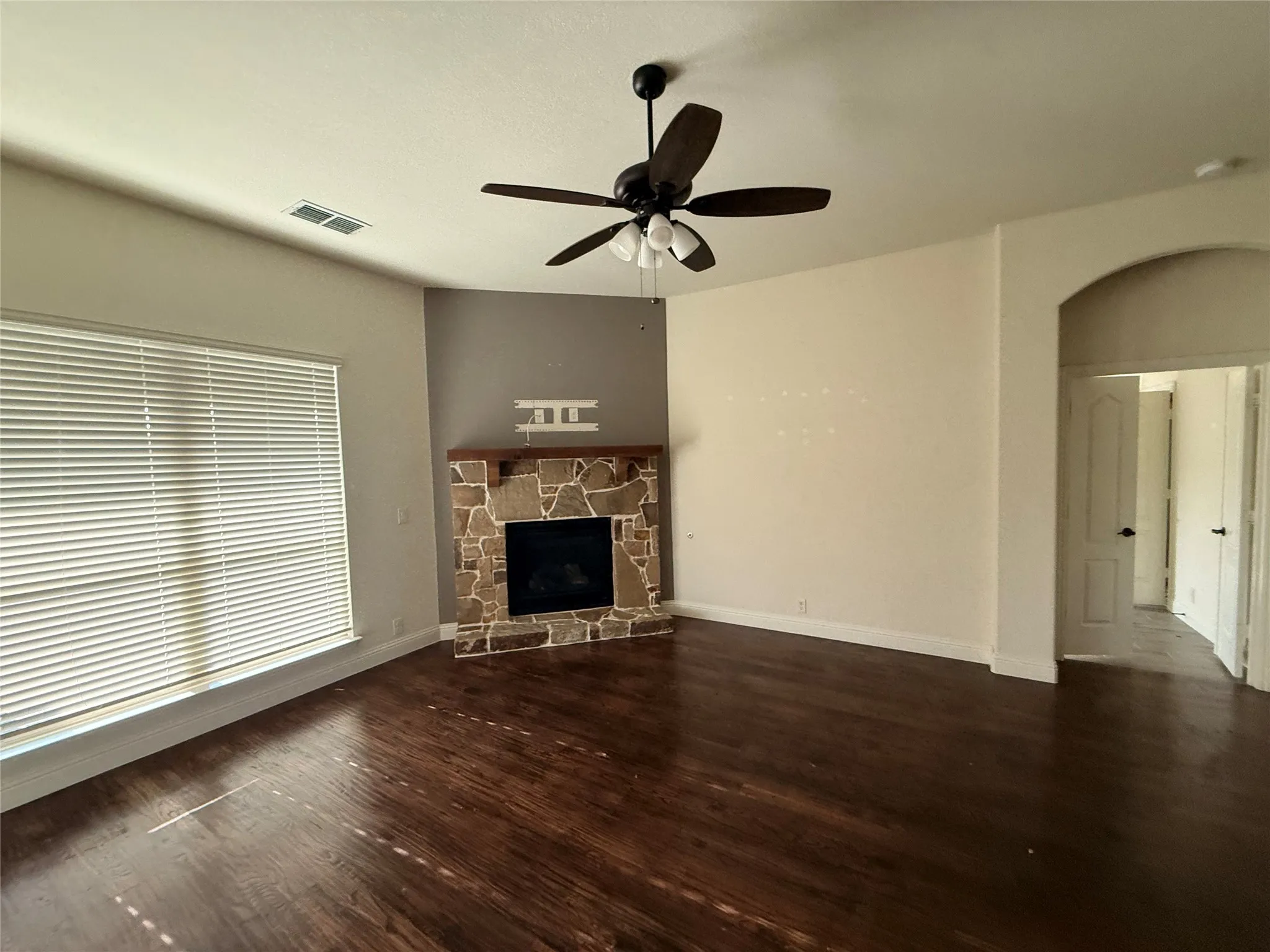 Wood-finish flooring, stone fireplace with a wood mantel, ceiling fan with integrated lighting, and an arched doorway