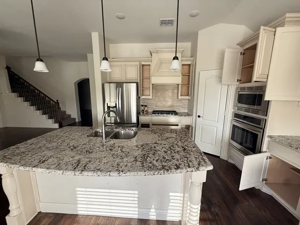 Kitchen island with a double basin sink, stainless steel appliances, wood-finish flooring, and pendant lighting