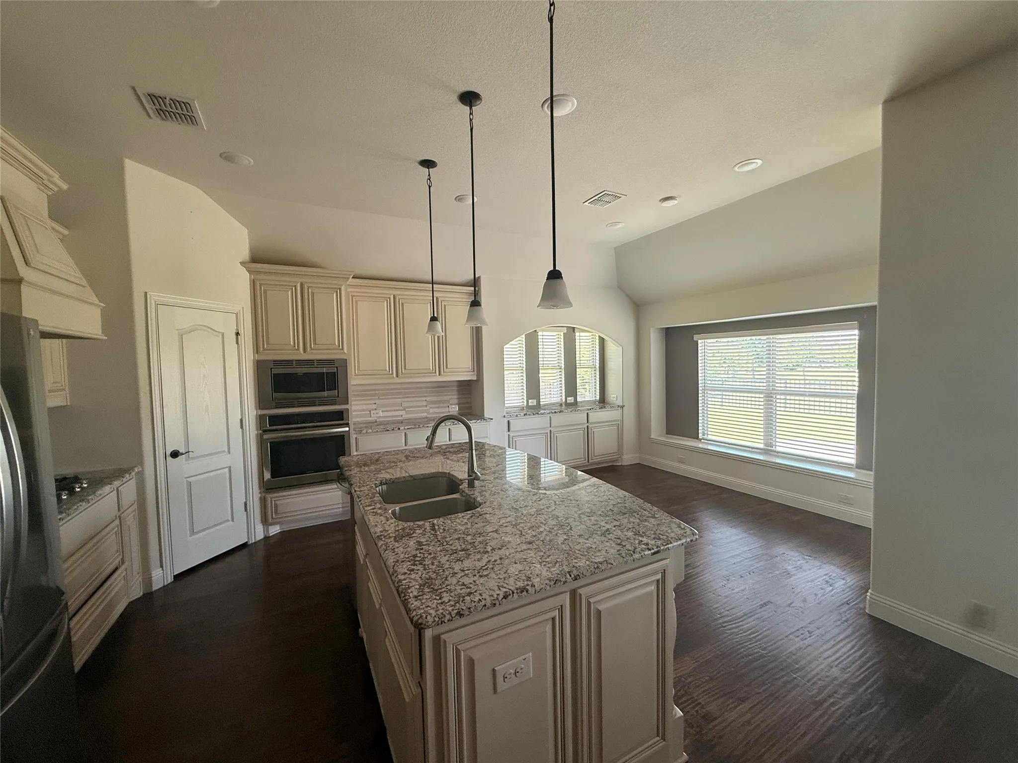 Kitchen featuring an expansive island with a double basin sink, light-toned cabinetry, integrated double ovens, and wood-finish flooring